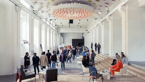 Een ruime binnenruimte met hoge plafonds, grote ramen en een centrale trap.