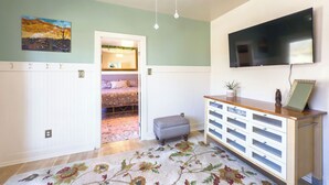 A bedroom with a bed, a dresser, a TV, and a painting on the wall.