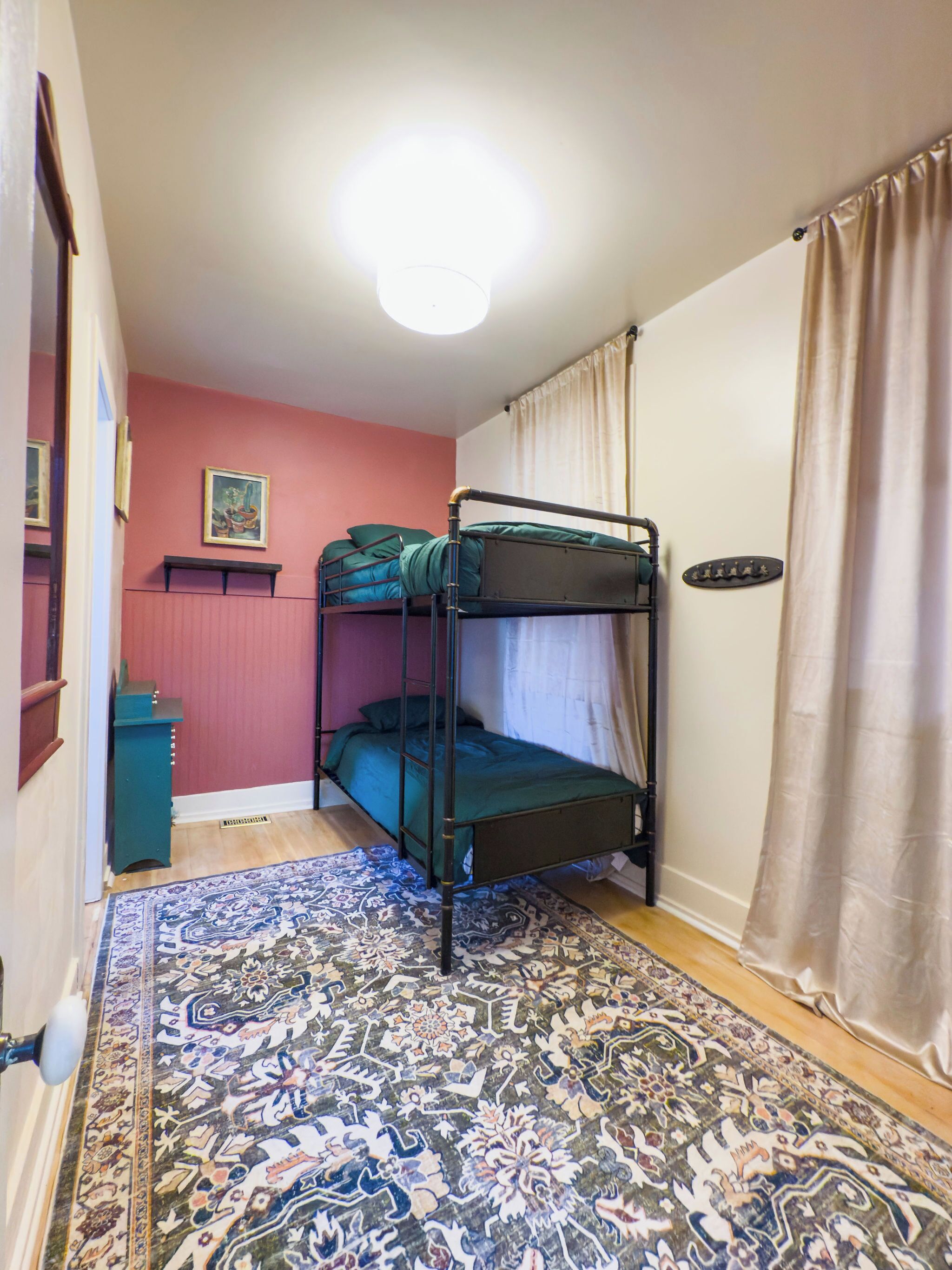 Habitación con literas, un tapete estampado, un estante pequeño y un cuadro en la pared.