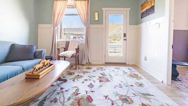 A living room with a sofa, a wooden coffee table, a chair with a blanket, a door with a view, and a painting on the wall.