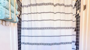 A bathroom with a patterned shower curtain, a green mat, and a tiled floor.