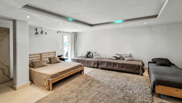 A modern bedroom with a large bed, two smaller beds, a ceiling projector, and a view of the outside.