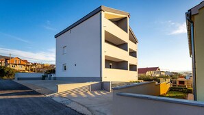 Un edificio moderno de dos pisos con techo plano, un balcón en el segundo piso y una ventana pequeña en la planta baja.