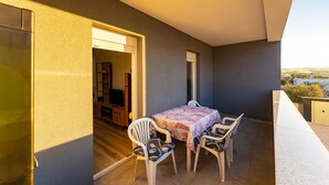 Un balcón con mesa y sillas, una puerta que da a una habitación interior y vistas del paisaje.