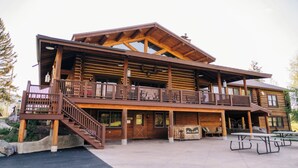 A wooden lodge with a balcony, outdoor seating, and picnic tables.