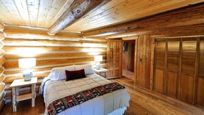 A log cabin bedroom with a bed, bedside tables, and a wooden wardrobe.