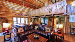 A log cabin interior with a leather sofa, wooden floors, and mounted animal heads.