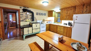 A kitchen with wooden cabinets, a stove, a sink, and a refrigerator. - Historic Pioneer Cabin (Coram)