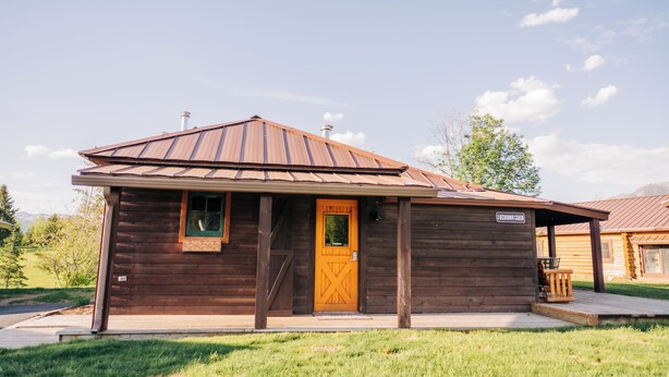 A rustic wooden cabin with a brown door and a small porch. - Historic Pioneer Cabin (Coram)