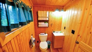 A wooden cabin bathroom with a toilet, sink, and shelves with toiletries.