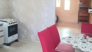 Uma cozinha com fogão branco, uma cadeira vermelha e uma mesa com toalha de mesa florida.