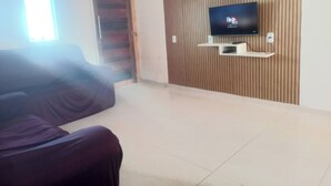 Sala de estar com televisão de tela plana fixada em uma parede revestida de madeira, um sofá e uma porta que dá para outro cômodo.
