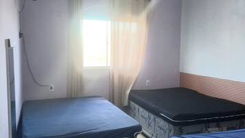 Quarto com duas camas, janela com cortinas, ventoinha e luminária.