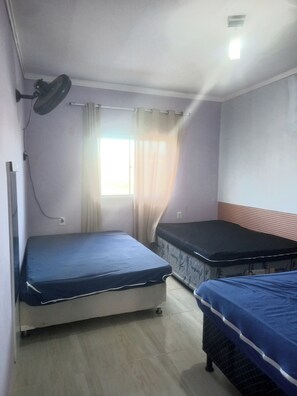 A room with two beds, a window with curtains, a standing fan, and a light fixture. - Sophia's beach house (Estância)