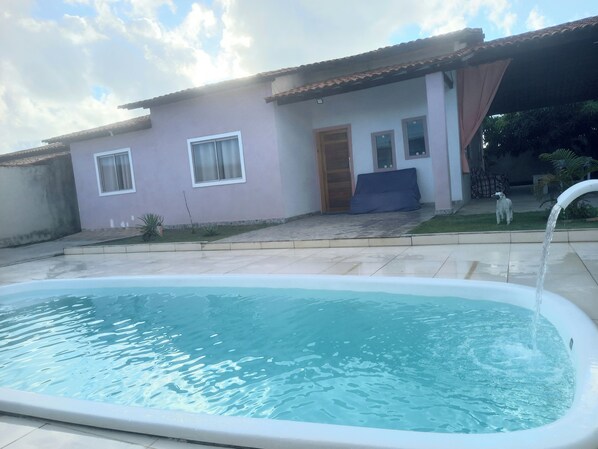 A swimming pool with a tiled deck, a house with a tiled roof, and a small dog in the background. - Sophia's beach house (Estância)