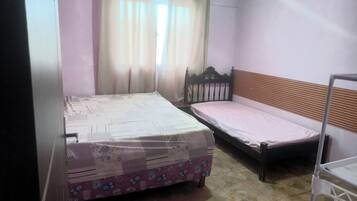 Quarto com duas camas, janela com cortinas, chão em azulejo e prateleira de metal.