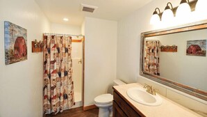 Ein Badezimmer mit Duschvorhang mit landwirtschaftlichen Motiven, einer weißen Toilette, einem Waschbecken mit Spiegel und einer Deckenleuchte.
