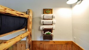 Eine Raumecke mit einem hölzernen Etagenbett, einem an der Wand befestigten Handtuchhalter mit Handtüchern und einem kleinen Regal mit einem grünen Handtuch, sowie einer Wandleuchte.