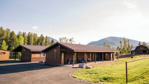 Ein rustikales Blockhaus mit überdachter Veranda und Sitzgelegenheiten im Freien, umgeben von einer Wiese und Bergen.