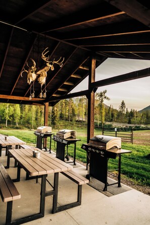 Un espace extérieur abrité comprenant des tables de pique-nique, des barbecues et une sculpture représentant la tête d’un cerf.
