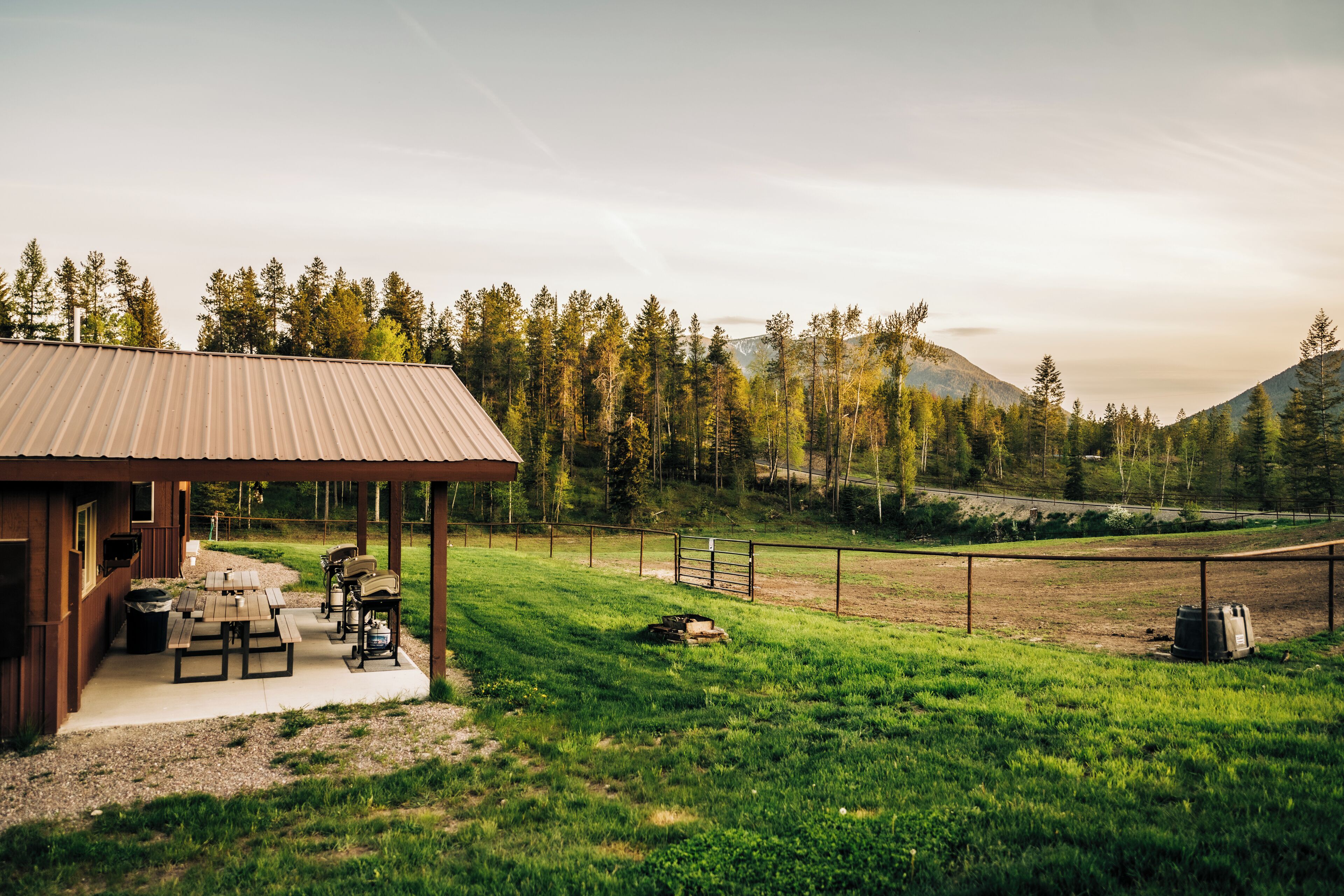 A rustic cabin with a covered patio, picnic tables, and a barbecue grill.