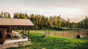 A rustic cabin with a covered patio, picnic tables, and a barbecue grill.