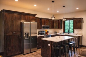 A modern kitchen with dark wooden cabinets, stainless steel appliances, a central island with bar stools, and pendant lighting.