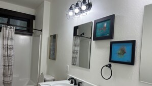 Une salle de bain avec un lavabo blanc, deux miroirs, un porte-serviettes et un rideau de douche.