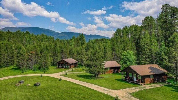 A lodge with three cabins surrounded by a forest, a clear sky, and distant mountains.