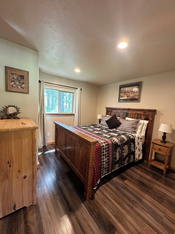 Un dormitorio con cama de madera, mesita de noche, cómoda, ventana con cortinas y una lámpara en el techo.