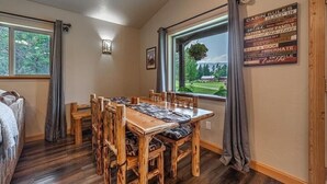 A cozy cabin-style room with a wooden dining table and chairs, a large window with a view of the outdoors, and a wall-mounted sign with cabin rules.