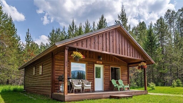 A wooden cabin with a porch, two chairs, and a table.