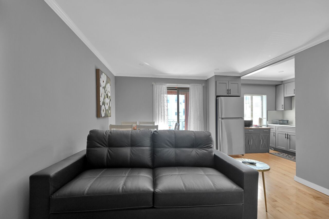 Una sala de estar moderna con un sofá de cuero gris, una mesita redonda y vistas al área de la cocina.