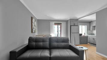 Una sala de estar moderna con un sofá de cuero gris, una mesita redonda y vistas al área de la cocina.