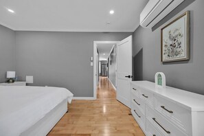 A modern bedroom with a large bed, a dresser, and a framed artwork on the wall.