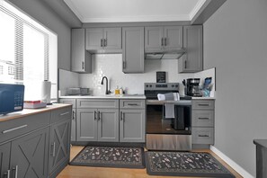 A compact kitchen with grey cabinets, a stainless steel stove, and a window with blinds.