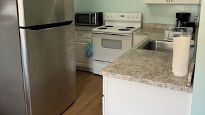A compact kitchen with a stainless steel refrigerator, a microwave, an oven, and a sink.
