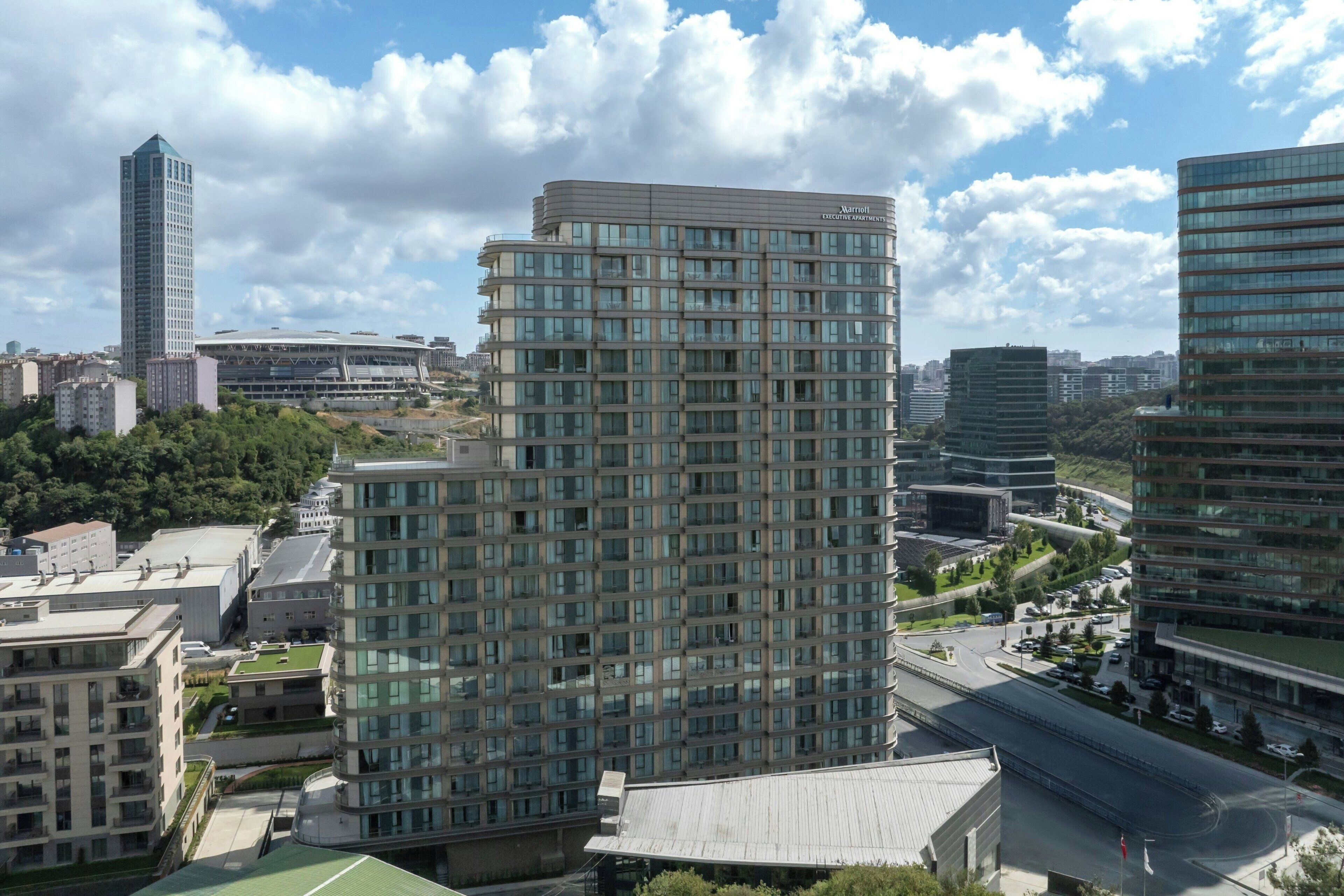 A modern high-rise building with a glass facade, surrounded by other high-rise buildings and a clear sky.
