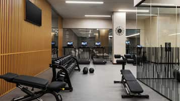 A modern gym with exercise equipment, benches, and a mirrored wall.