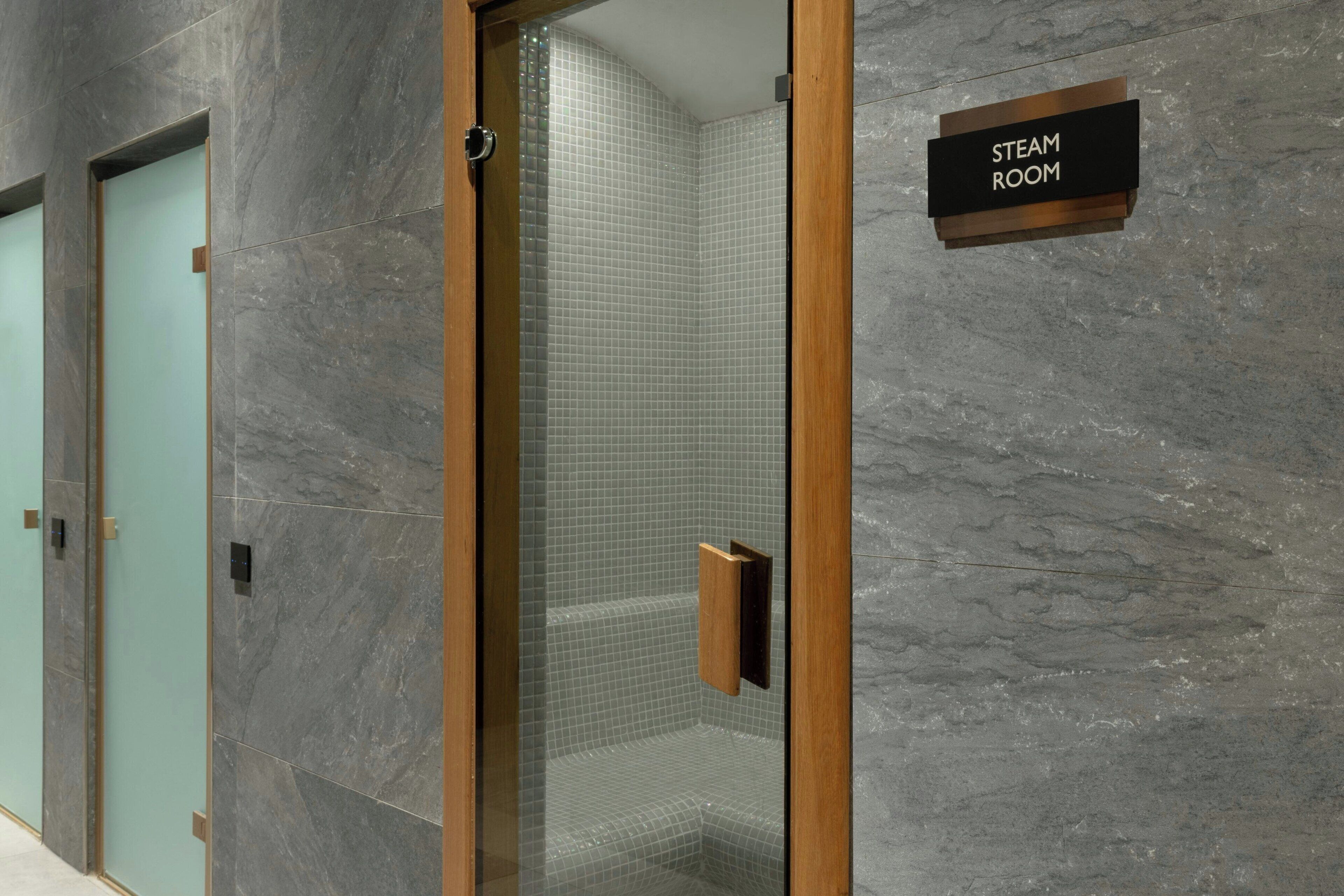 A modern bathroom with a glass-enclosed shower, a wooden door, and a sign indicating it's the steam room.