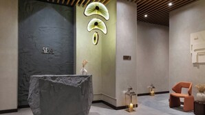 Un área de spa con mostrador de recepción de piedra, una lámpara de pared y una pequeña silla naranja.