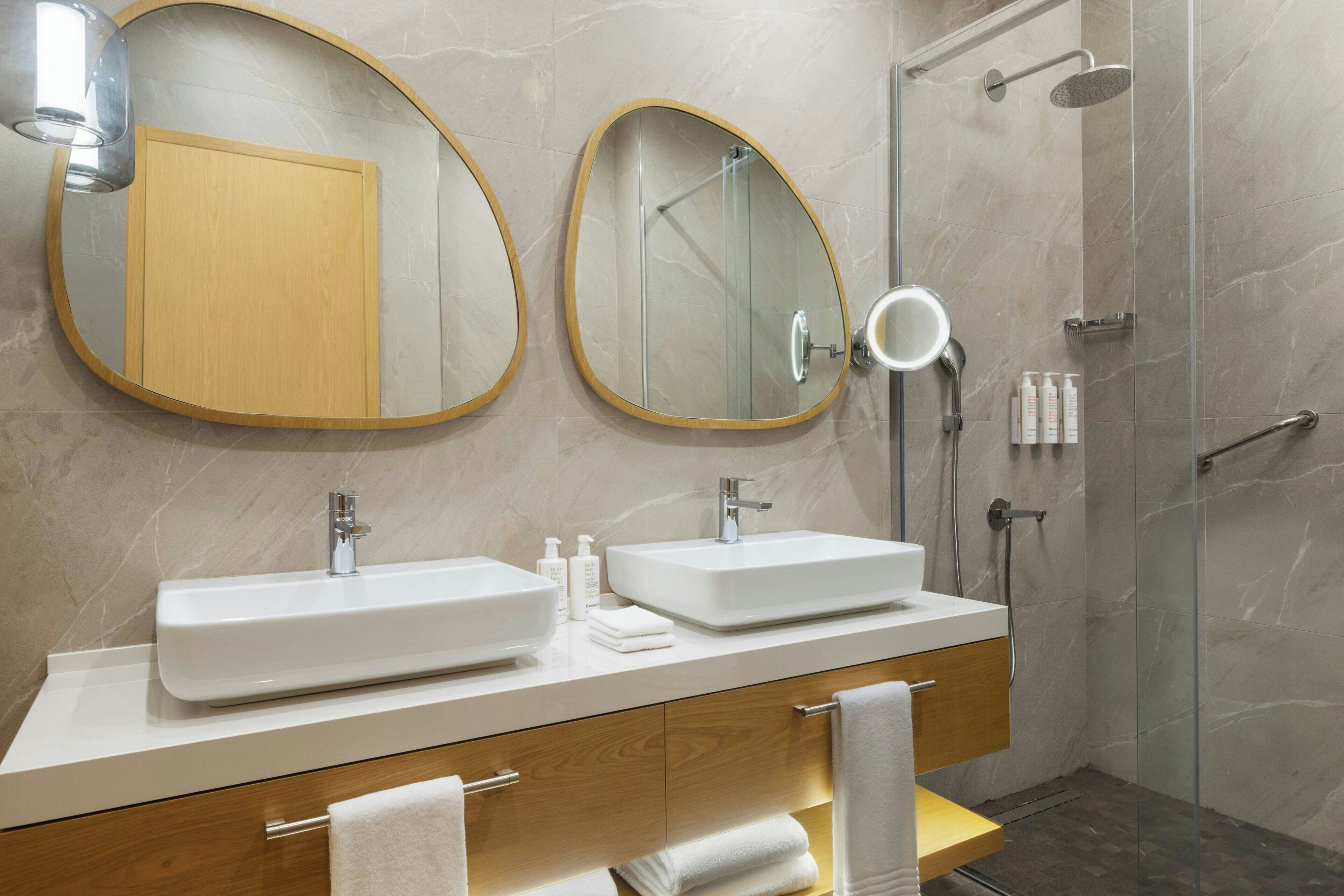 Un baño moderno con dos lavamanos, una ducha y un tocador con espejo.