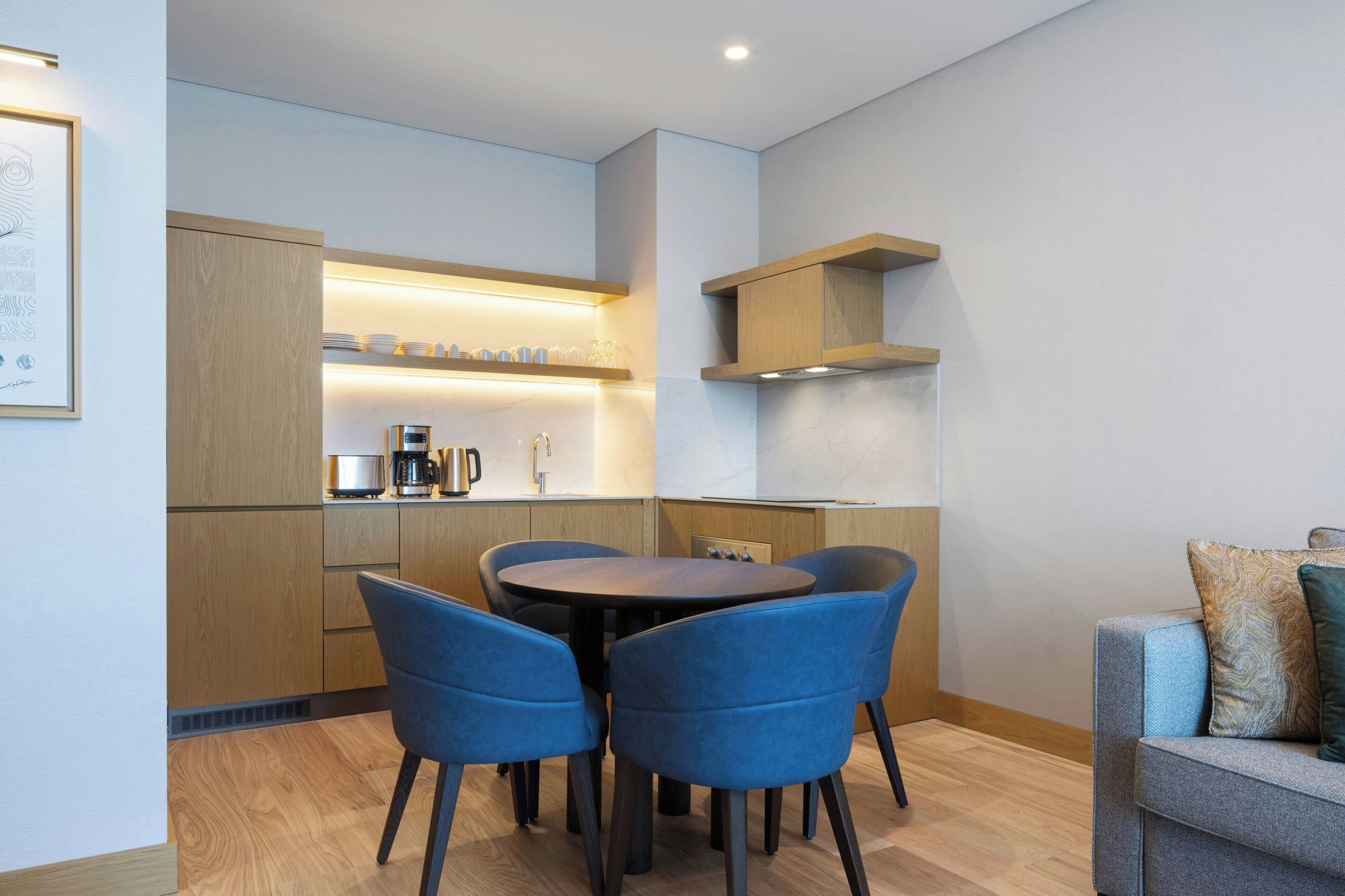 A modern kitchen with wooden cabinets, a dining table with blue chairs, and a built-in oven.