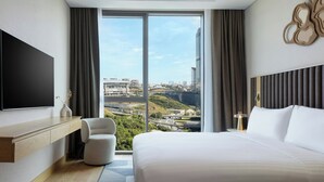 Una habitación de hotel moderna con una cama grande, un televisor de pantalla plana, un espacio de descanso y vistas a la ciudad.