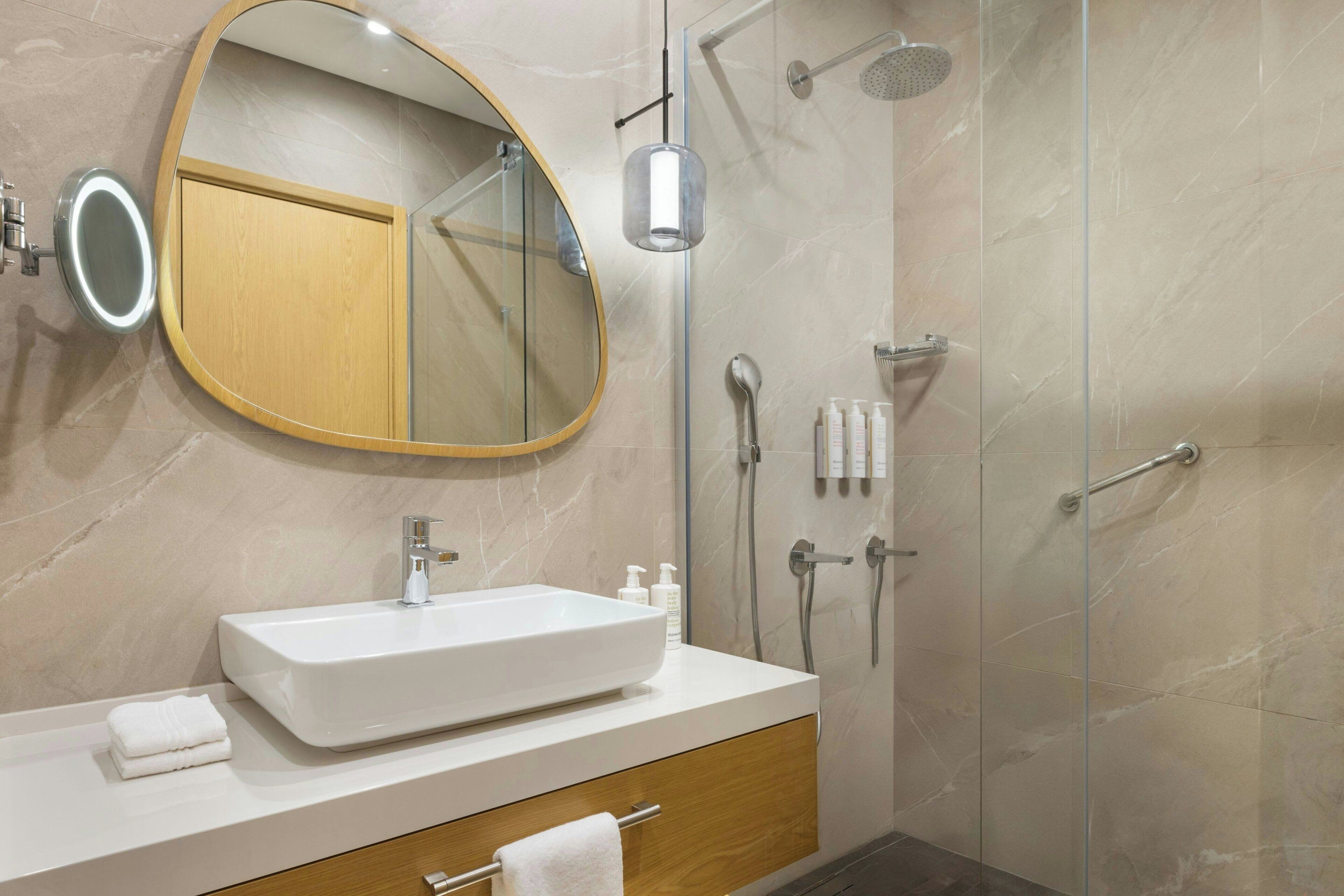 A modern bathroom with a large oval mirror, a rectangular sink, and a glass-enclosed shower.