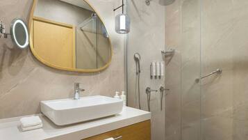 A modern bathroom with a large oval mirror, a rectangular sink, and a glass-enclosed shower.