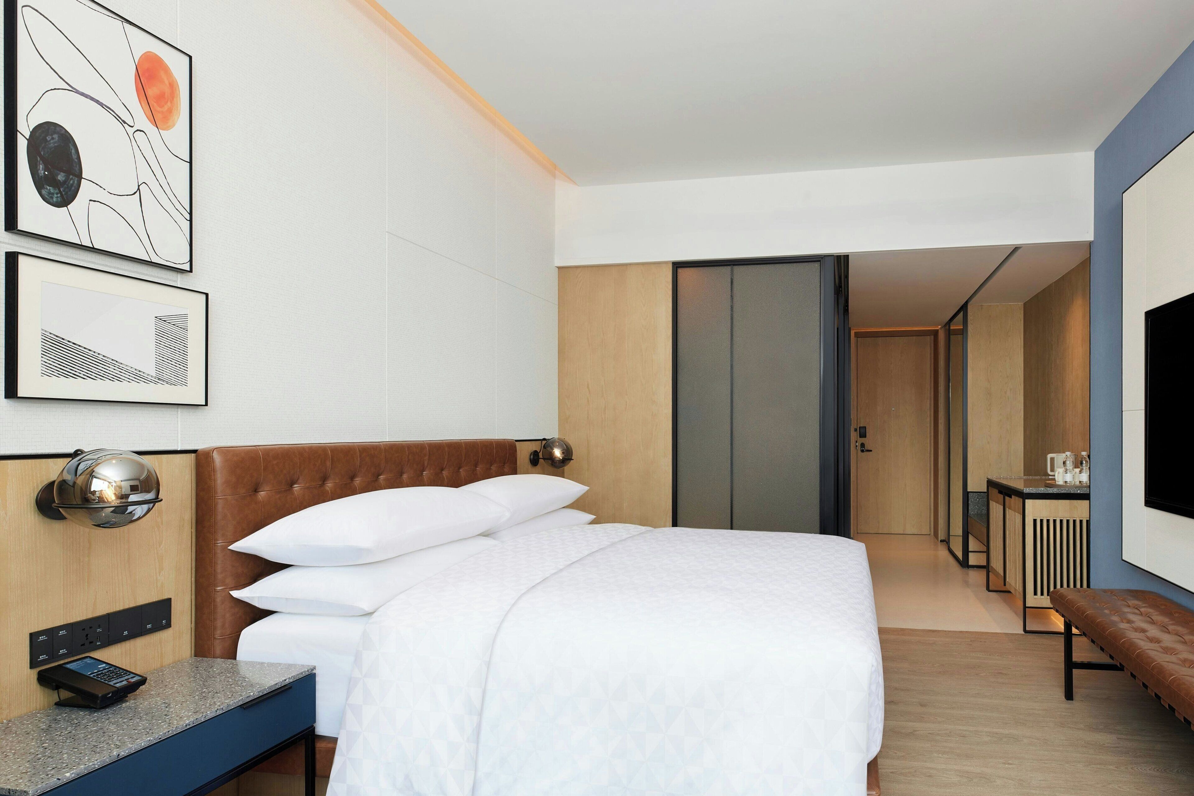 Una habitación de hotel moderna con una cama grande, un escritorio con una computadora, un televisor de pantalla plana y obras de arte en la pared.