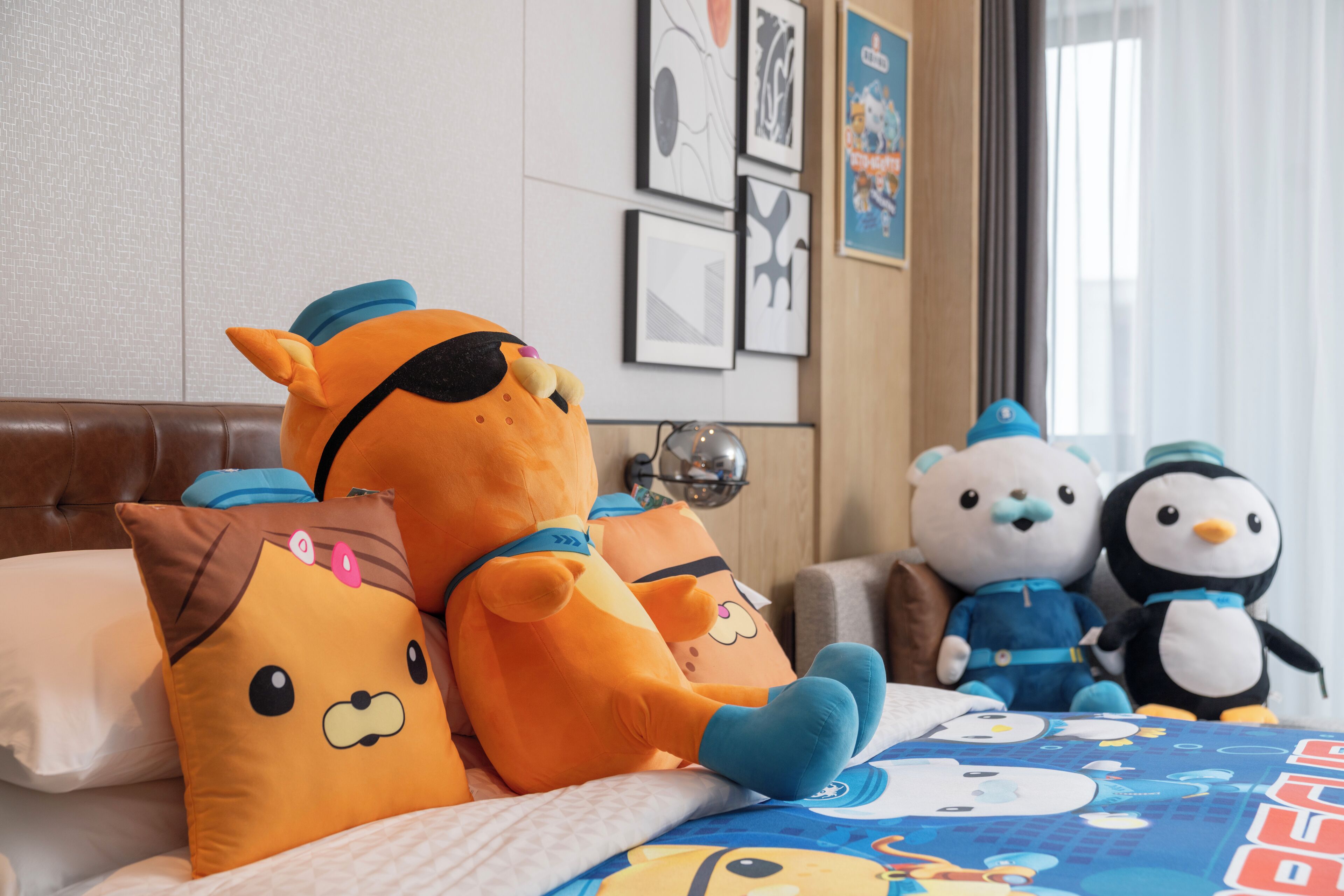 A bed with plush toys, a pillow, and a wall with framed pictures.