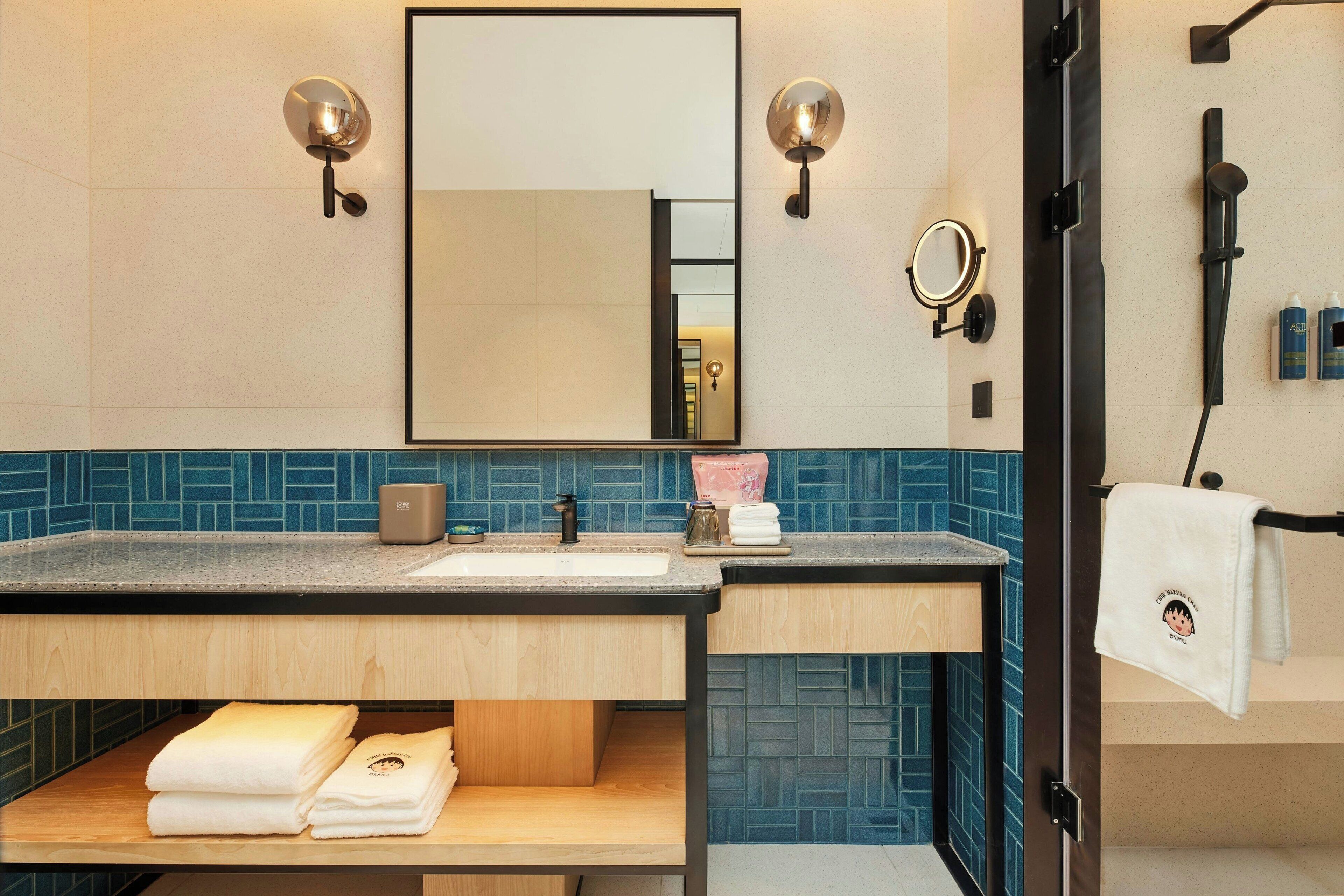 A modern bathroom with a wooden vanity, a large mirror, wall-mounted lights, and a towel rack.
