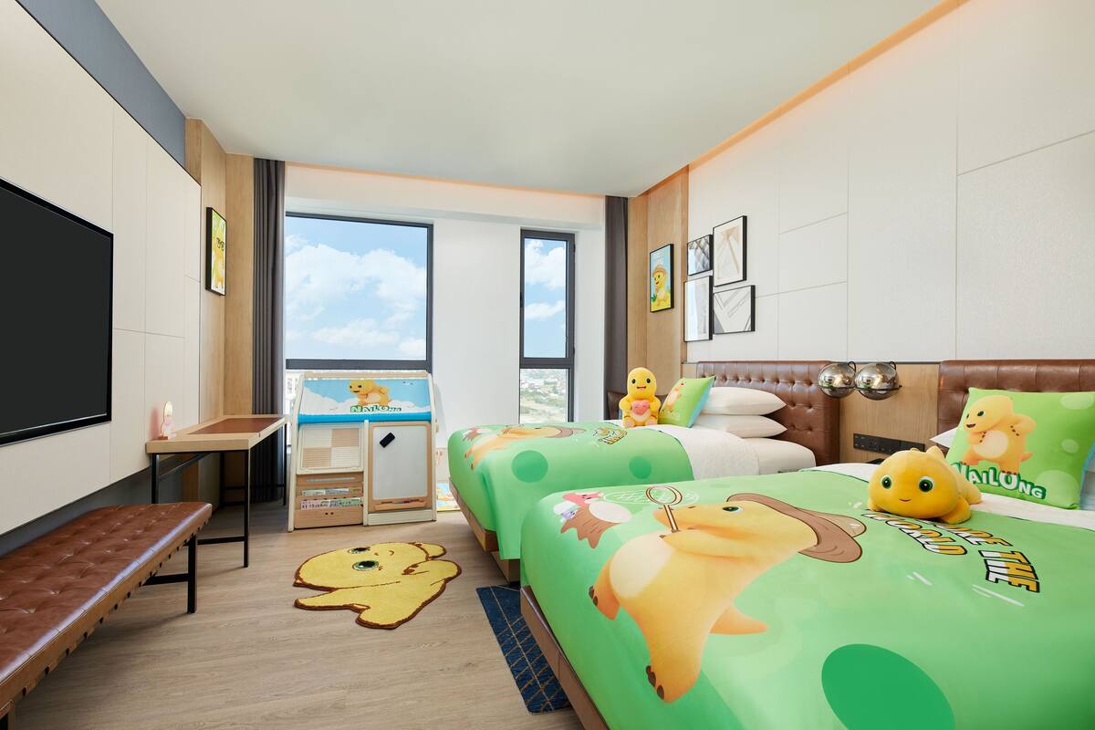 A hotel room with two beds, a desk, a TV, and a large window.